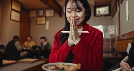 Téléchargez les photos : Restaurant, prière et femme japonaise avec de la nourriture pour le déjeuner, le dîner et le souper à la cafétéria. Heureux, sourire et personne avec geste de la main de prière et baguettes pour manger le repas, le bien-être et la nutrition. - en image libre de droit