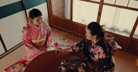 Foto de Las mujeres con la tradicional taza de té japonés, kimono y relajarse con atención plena, respeto y conversación. Amigos en salón de té tranquilo con bebida matcha, cultura zen asiática y ritual en la mesa para la ceremonia - Imagen libre de derechos