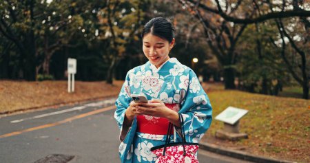 Foto de Ciudad, teléfono y mujer japonesa en la calle para la creación de redes en línea, sitio web y redes sociales. Viaje, caminata y persona feliz escribiendo en el teléfono inteligente con la moda tradicional, cultura y kimono en la naturaleza. - Imagen libre de derechos