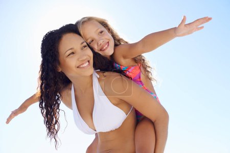 Photo for Happy mother, child and piggyback on beach for bonding, vacation or outdoor holiday weekend together. Mom, kid or daughter smile in sun for love, support or summer break with blue sky background. - Royalty Free Image