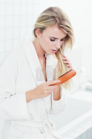 Photo for Woman, blonde and brushing hair for beauty, cosmetics or style in bathroom or keratin treatment at home. Face of attractive young female person in haircare with brush for knots or split ends at house. - Royalty Free Image