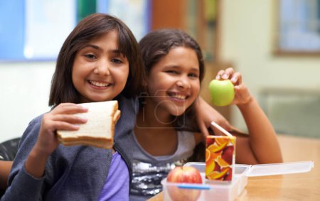 Photo for Girls, happy and portrait with lunch at school for recess, break or nutrition at table with diversity. Kids, face and smile at academy or relax with confidence, food or embrace for friendship or care. - Royalty Free Image