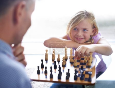 Téléchargez les photos : Sourire, enfant et père jouent aux échecs à la maison, en famille ou en développement. Happy girl, homme et jeu de société de stratégie, défi ou divertissement du jeune enfant en compétition match dans la maison. - en image libre de droit