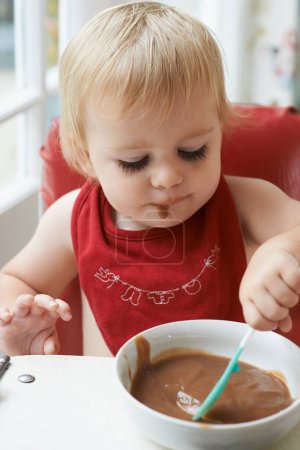 Photo for High chair meal, spoon and baby eating in a house with diet, nutrition and child, wellness or development. Food, messy eater and boy kid curious about breakfast porridge, playing or learning at home. - Royalty Free Image