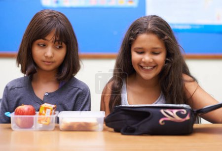 Foto de Niños felices, estudiantes y comer alimentos en el aula de la escuela para la comida, descanso o merienda. Niñas pequeñas o niños de primaria sonríen con una bolsa de almuerzo para la salud, la nutrición o las vitaminas en clase. - Imagen libre de derechos