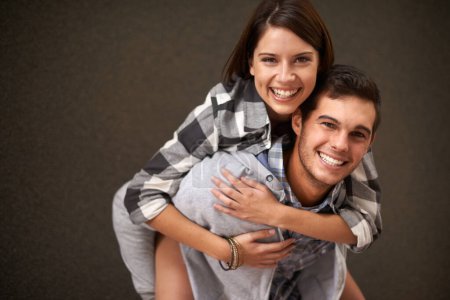 Photo for Studio, hug and portrait of happy couple, piggyback ride and having playful fun together on brown background. Wellness, embrace and young silly man, woman or people smile for goofy game. - Royalty Free Image