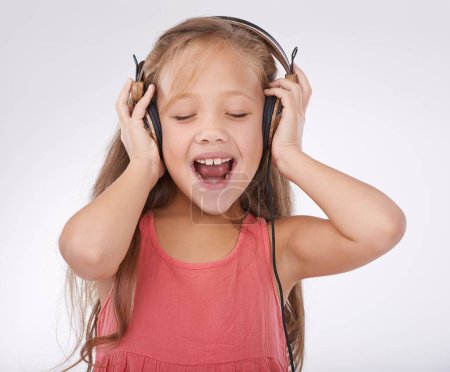 Photo for Girl kid, music and singing with headphones in studio for audio, subscription and streaming multimedia on white background. Happy child, shouting and listening to podcast, hearing sound and radio. - Royalty Free Image