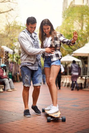Téléchargez les photos : Promenade en skateboard, heureux et couple enseigner à la petite amie comment équilibrer, leçon d'exercice ou de formation dans l'Espagne urbaine. Skate, fun et skateboarder aider, coaching et sourire pour le développement du skateboard. - en image libre de droit