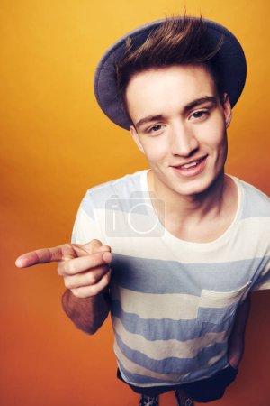 Photo for Portrait, hipster and man with fashion, pointing and confident guy on an orange studio background. Person, hand gesture and model with stylish clothes, hat and casual outfit with aesthetic and trendy. - Royalty Free Image