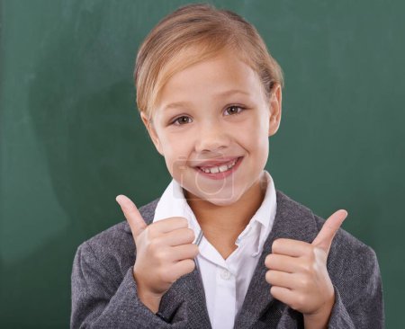 Photo for Child by chalkboard, portrait and thumbs up for education, learning and school success, like and support. Face of happy kid, girl or student with good job, yes or ok hands for classroom achievement. - Royalty Free Image