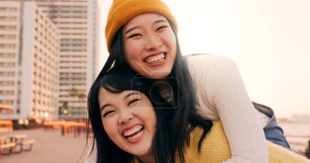 Photo for Friends, women and piggyback outdoor on promenade with bonding, laughing and adventure on holiday or vacation. Travel, Japanese people or embrace at beach in city with fun, comedy or freedom together. - Royalty Free Image