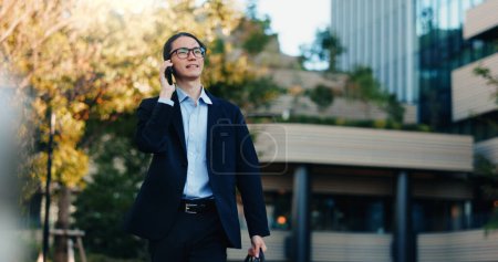 Photo for Phone call, walking and business man on city journey, morning travel and speaking on mobile discussion. Smartphone conversation, communication and Japanese agent talking with contact on urban commute. - Royalty Free Image