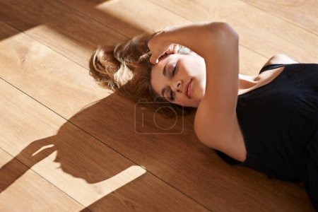 Foto de Casa, piso de madera y mujer en sol con belleza o y resplandor en la piel en Suiza apartamento. Calma, persona y chica tumbada con sombra en el suelo en casa y relajarse en el salón con vitamina d. - Imagen libre de derechos