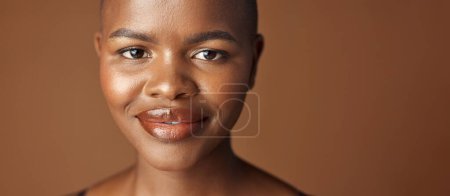 Téléchargez les photos : Visage, beauté et sourire avec une heureuse femme noire en studio isolée sur fond brun pour le bien-être. Portrait, soins de la peau et esthétique pour les cosmétiques de fond de teint ou la dermatologie avec une personne chauve naturelle. - en image libre de droit
