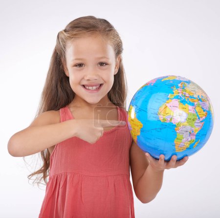 Photo for Kid, pointing to globe in studio with world, planets and city for education, geography and portrait. Student, girl child and travel map with smile for earth day support or ecology on white background. - Royalty Free Image