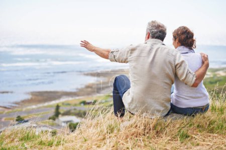 Photo for Old couple and pointing at nature on holiday, vacation or embrace with love or support in retirement. Back, man and woman together sightseeing on hill at beach or relax in environment and adventure. - Royalty Free Image