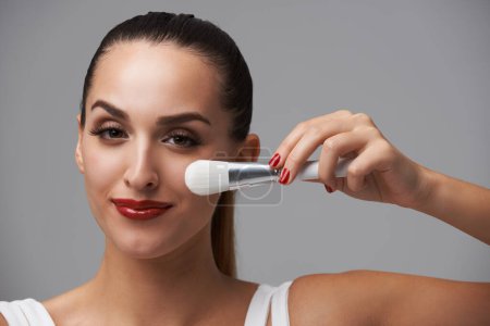 Photo for Woman, face and brush for makeup, beauty and red lipstick with manicure and cosmetic tools on grey background. Portrait, equipment with color nails and lips, foundation or powder with smile in studio. - Royalty Free Image