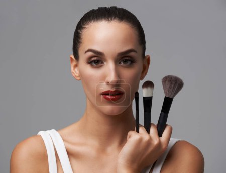 Photo for Woman, brush for makeup and beauty in portrait, cosmetic tools with cosmetology and skin on grey background. Red lipstick, confidence and face of model in studio, foundation or powder with equipment. - Royalty Free Image