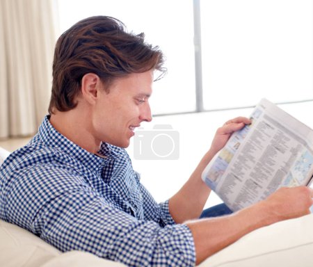 Photo for Man, newspaper and reading on sofa with article for story, relax or information with smile in living room. Person, news and morning routine on couch with print media or knowledge for break in lounge. - Royalty Free Image