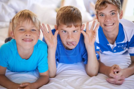 Photo for Silly, funny and boy children on bed bonding for joke with comic, goofy and comedy faces. Happy, excited and portrait of young kids with crazy and playful facial expression in bedroom at modern home - Royalty Free Image
