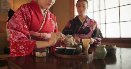 Téléchargez les photos : Traditionnel, théière et femmes japonaises avec du thé pour la culture avec des herbes, des feuilles et de la saveur à la maison. Rituel, indigènes et les gens avec des boissons à base de plantes pour le calme, cérémonie et boire pour le bien-être. - en image libre de droit