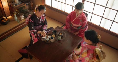 Téléchargez les photos : Japonais, femmes et kimono pour la cérémonie du thé à Chashitsu avec matcha ou tradition coutumière. Personnes, temae et robe de style vintage ou vue de dessus pour la culture, la mode et l'honneur avec vaisselle antique. - en image libre de droit