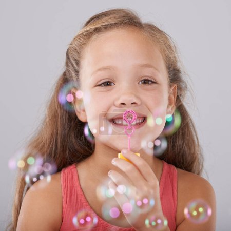 Photo for Portrait, kid and blowing bubbles in studio by toy, happiness and fun games for hand eye coordination. Little girl, face and learning to play on soap wand, development and sweet by gray background. - Royalty Free Image