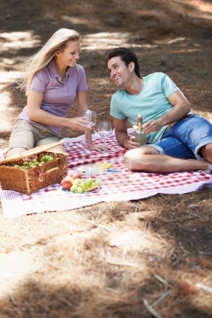 Photo for Couple, picnic and champagne in forest with love, romantic celebration and summer date on valentines day. Young people with food, fruits and bottle with wine glasses in woods or nature on anniversary. - Royalty Free Image
