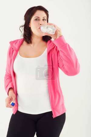 Photo for Woman, portrait and drinking water in fitness for hydration after workout or exercise on a white studio background. Thirsty female person with mineral drink in natural sustainability on break or rest. - Royalty Free Image