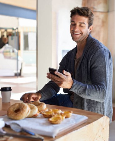 Foto de Teléfono, sonrisa y hombre con desayuno en la red de restaurantes en las redes sociales, aplicación móvil o Internet. Feliz, comida y joven hombre desplazarse en el teléfono celular con comida saludable en la cafetería o cafetería - Imagen libre de derechos