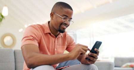 Téléchargez les photos : Heureux, tapant et un homme noir avec un téléphone sur le canapé pour les médias sociaux, connexion ou communication. Souriez, détendez-vous et une personne africaine avec un mobile pour une application, un e-mail ou une notification dans une maison. - en image libre de droit