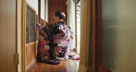 Foto de Puerta abierta, mujer japonesa y cultura con kimono, respeto y relax en el alojamiento tradicional. Mañana, casa y arrodillarse en una ventana con zen, arquitectura tranquila y antigua con vestido antiguo. - Imagen libre de derechos