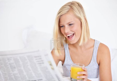 Photo for Happy woman, orange juice and reading newspaper on bed for headlines, energy and health body with wellness. Blonde hair, lady and thirsty for glass of fruit drink, morning and vitamin c with smile. - Royalty Free Image