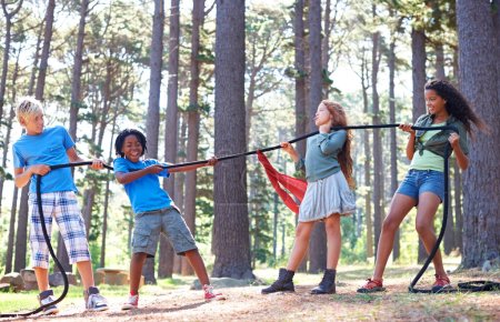 Téléchargez les photos : Enfants, corde et remorqueur de guerre pour jouer à l'aventure, défi et jeu de force dans les bois avec camping d'été. Enfants, diversité et compétitivité dans l'environnement forestier et travail d'équipe dans le rapport de force par les arbres. - en image libre de droit