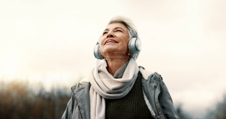 Photo for Headphones, music and senior woman in nature for wellness, mental health and happy outdoor experience. Travel, listening and streaming service or podcast of elderly person thinking in park and winter. - Royalty Free Image