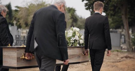 Photo for Coffin, men and pallbearers walking at graveyard ceremony outdoor at burial tomb. Death, grief and group casket at cemetery, carrying to funeral and family service of people mourning at windy event. - Royalty Free Image