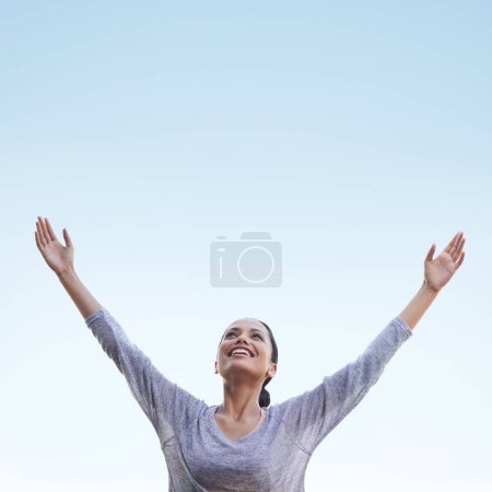 Foto de Mujer, brazos arriba y cielo azul con libertad y felicidad al aire libre, salud y bienestar, alivio del estrés y la gratitud, Celebración, alegría y sonrisa en la cara en la naturaleza con espacio de maqueta, alabanza y agradecimiento. - Imagen libre de derechos