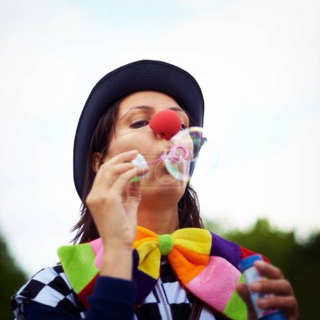 Téléchargez les photos : Clown soufflant des bulles au festival de plein air pour le plaisir, la fantaisie et l'aventure estivale dans la nature. Visage d'une personne, d'un artiste de rue ou d'un personnage de cirque dans un parc avec une couleur créative lors d'un heureux carnaval - en image libre de droit