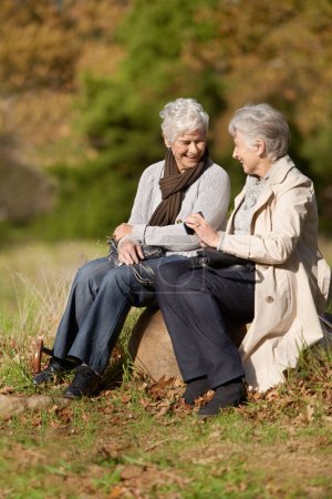 Photo for Senior women, laughing or conversation in nature for travel, together or bonding on retirement in outdoor. Elderly friends, smile or communication on vacation in countryside, care or social on rock. - Royalty Free Image