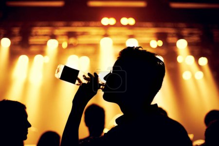 Photo for Night, club and man with a drink at party, event or music festival with stage lights and silhouette. Dark, concert and person dance with bottle of alcohol in crowd at social celebration or rave. - Royalty Free Image