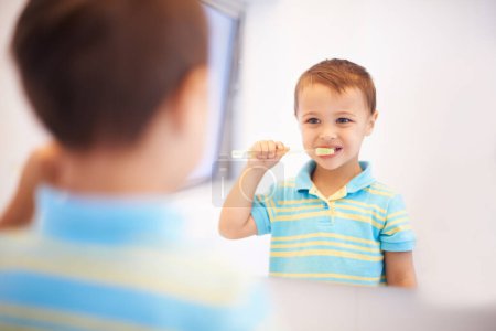 Foto de Niño niño, cepillarse los dientes y espejo en el baño para la limpieza, higiene o salud para la rutina en el hogar. Niño, cepillo de dientes o reflexión para el bienestar dental, sonrisa o resultados en la mañana en la casa de la familia. - Imagen libre de derechos