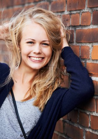 Photo for Beauty, portrait and woman with hair by brick wall in city, smile or happy outdoor. Face, fashion and hairstyle of young person in casual clothes, facial expression and blonde girl in Switzerland. - Royalty Free Image
