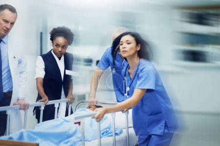 Photo for Rushing to the ER. Shot of a group of medical professionals rushing a patient on a gurney down a hospital corridor - Royalty Free Image