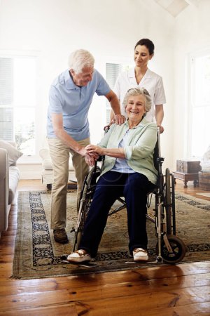 Foto de Rodeado de apoyo. Fotografía de un cuidador sonriente con una mujer mayor en silla de ruedas y su marido en casa - Imagen libre de derechos