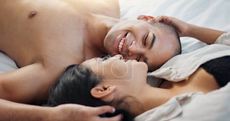 Téléchargez les photos : Couple heureux, parlant au lit avec amour, intimité et romance à la maison pour la relation, le sexe et les liens. Les jeunes, la femme et l'homme se détendent dans la chambre avec un toucher doux et baiser pour la Saint-Valentin. - en image libre de droit