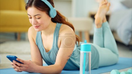 Photo for Smartphone, yoga and headphones of woman typing on chat app for fitness communication, social media update or blog writing wellness. Pilates girl with exercise gear and technology in home living room. - Royalty Free Image