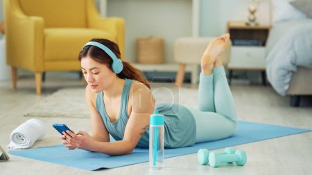 Photo for Smartphone, yoga and headphones of woman typing on chat app for fitness communication, social media update or blog writing wellness. Pilates girl with exercise gear and technology in home living room. - Royalty Free Image