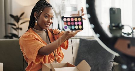 Téléchargez les photos : Vidéo, créateur de contenu et femme noire faisant maquillage pour tutoriel sur les médias sociaux ou Internet. Cosmétique, heureuse et jeune femme africaine influenceuse film ou flux en direct visage routine de cosmétologie à la maison - en image libre de droit