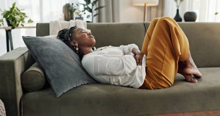 Photo for Home, pain and black woman on a couch, cramps and stomach with sickness, suffering and disease in the living room. African person, apartment and girl with abdominal problem, tummy ache and period. - Royalty Free Image