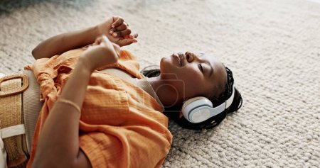 Foto de Auriculares, relax y mujer joven en el suelo en la sala de estar escuchando música o radio en el apartamento moderno. Baile, sonrisa y joven mujer africana streaming canción en el salón en casa - Imagen libre de derechos